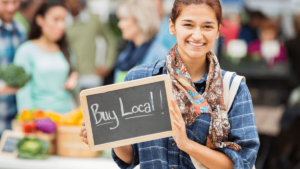 Smiling person holding Buy Local sign at farmers market