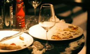 Messy restaurant table with empty wine glass, plates, pizza leftovers, pepper mill