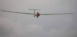 Front view T-tail sailplane glider with long wingspan and red nose in cloudy sky